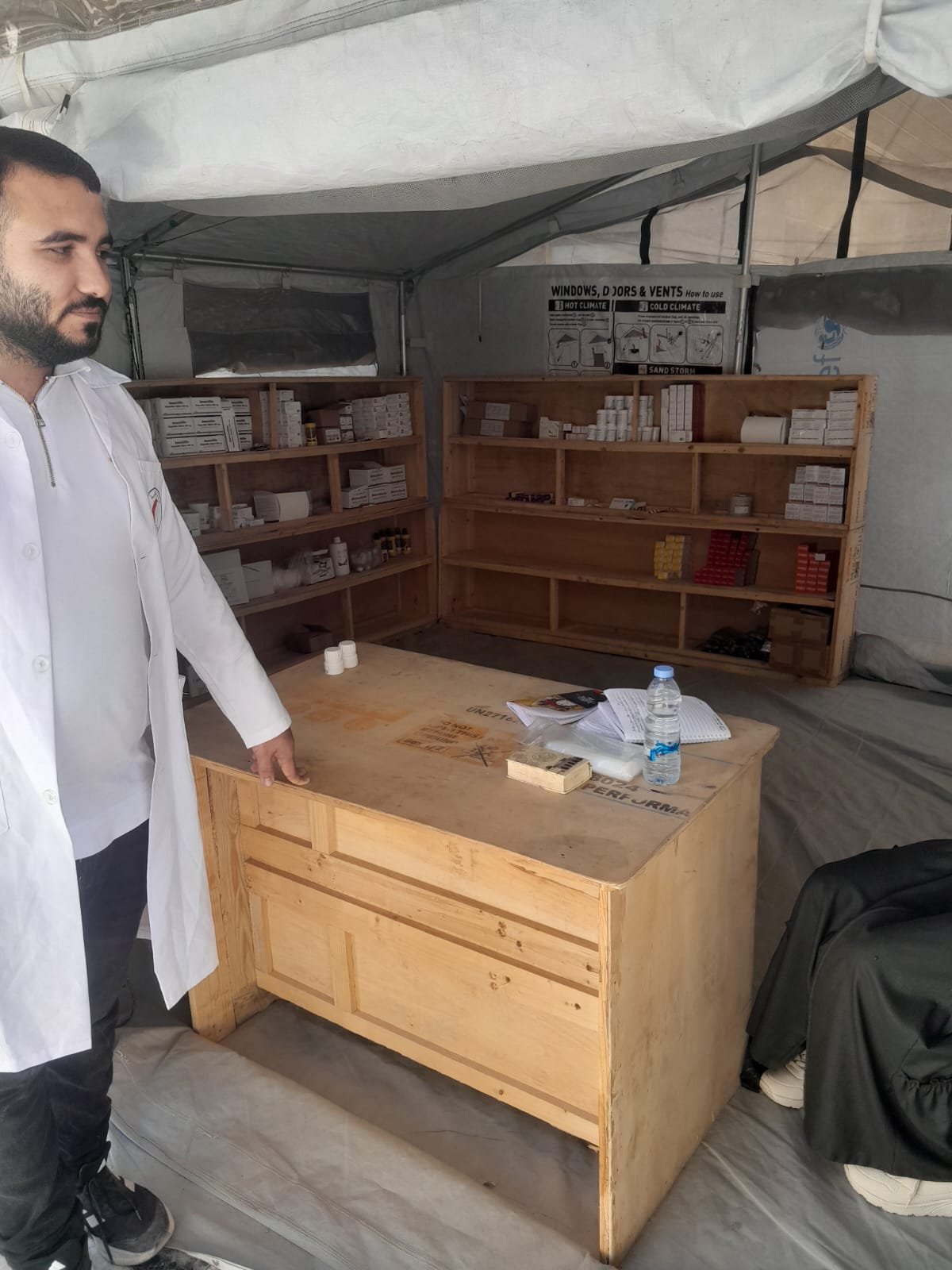 From the Ground Up: Building Al-Lababidi Clinic in Gaza Staff member and medicine shelves inside the clinic pharmacy tent