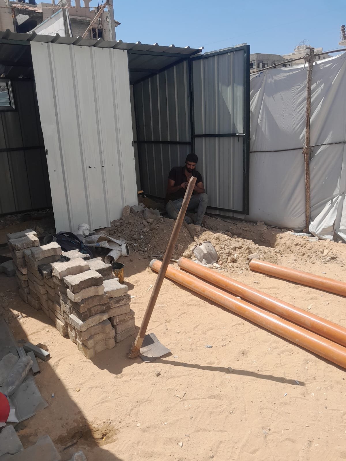 From the Ground Up: Building Al-Lababidi Clinic in Gaza Worker installing sanitation infrastructure beside a metal cubicle and exposed pipes